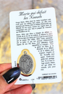 verso de la carte de prière de Marie qui défait les noeuds. Texte, prière à la sainte Vierge Marie. dos de la médaille intégrée. Carte tenue dans une main, fond doré et gris