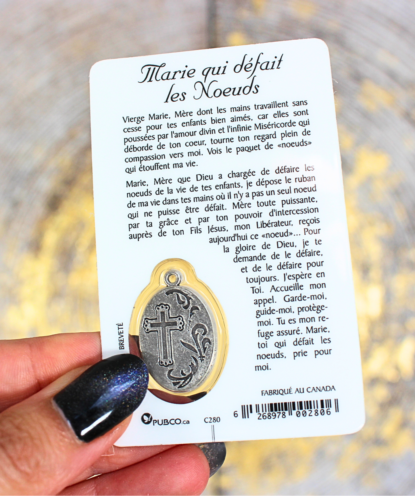verso de la carte de prière de Marie qui défait les noeuds. Texte, prière à la sainte Vierge Marie. dos de la médaille intégrée. Carte tenue dans une main, fond doré et gris