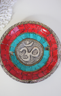 Apportez une énergie spirituelle unique à vos rituels avec ce porte-encens tibétain artisanal orné du symbole sacré Ôm.
Fabriqué à la main en Inde, il associe une mosaïque colorée (rouge, bleu profond, turquoise) et des détails en métal argenté et doré, faisant de chaque pièce une véritable œuvre d’art.