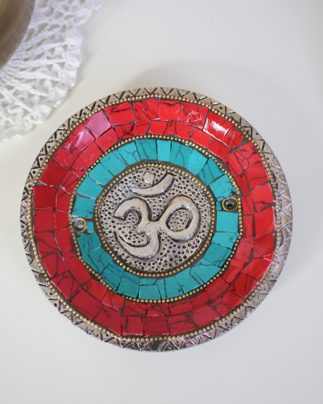 Apportez une énergie spirituelle unique à vos rituels avec ce porte-encens tibétain artisanal orné du symbole sacré Ôm.
Fabriqué à la main en Inde, il associe une mosaïque colorée (rouge, bleu profond, turquoise) et des détails en métal argenté et doré, faisant de chaque pièce une véritable œuvre d’art.