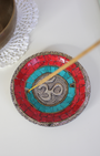Apportez une énergie spirituelle unique à vos rituels avec ce porte-encens tibétain artisanal orné du symbole sacré Ôm.
Fabriqué à la main en Inde, il associe une mosaïque colorée (rouge, bleu profond, turquoise) et des détails en métal argenté et doré, faisant de chaque pièce une véritable œuvre d’art.